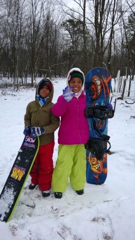 The kids grabbing their snowboards to enjoy the snowy downhill ride in the backyard of our Poconos home .